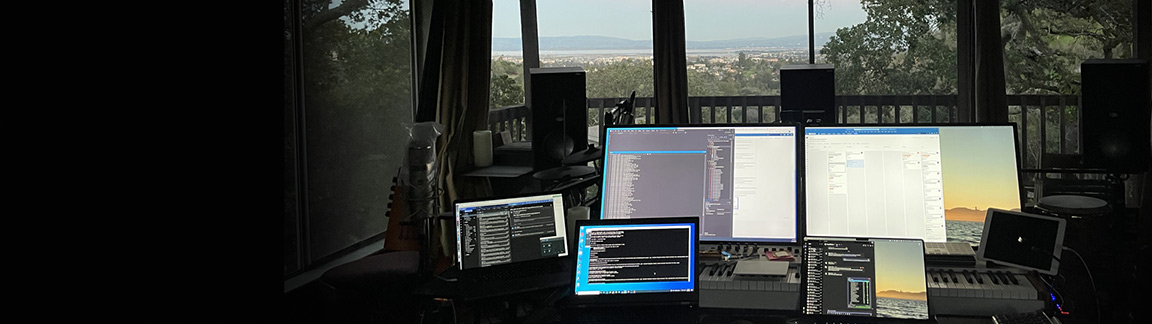 Control room at dusk, speakers and screens in front of a window wall over the bay and oak canopy.